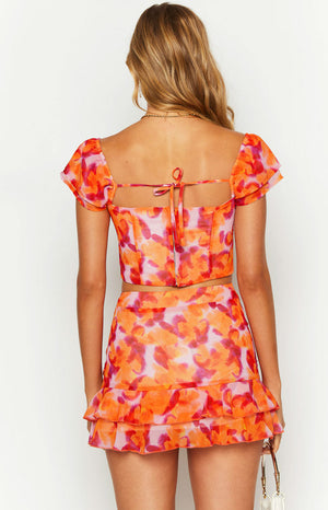 Rear view of an azalea pink print crop top with short flutter sleeves, tie-back, and exposed back zipper