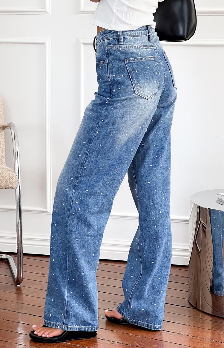 Side view of mid wash denim straight leg jeans covered in small rhinestones with visible back pockets