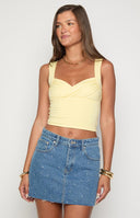 A person models a white halter top with a pink and orange floral pattern and a studded blue denim mini skirt. They accessorize with gold bracelets and rings and carry a white handbag.
