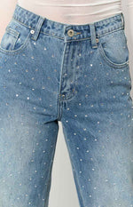 Close-up of the mid wash denim jeans showing all-over rhinestone studs, button fly, and front pockets