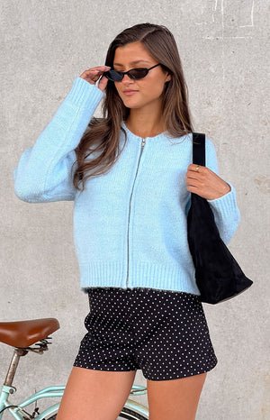 Our female model wearing a light blue zip-up knit cardigan with a round neckline and ribbed details your timeless look in your everyday errands.