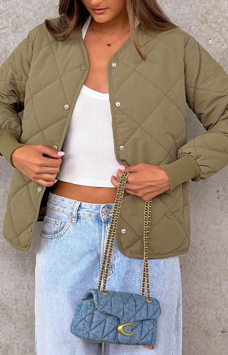 Khaki quilted bomber jacket with a collarless neckline and snap button front, worn open over a white top