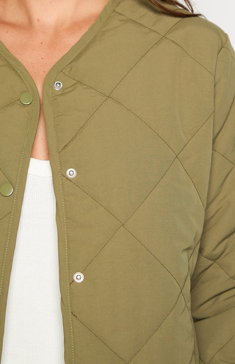 Close-up of the khaki quilted bomber jacket showing the snap button closure and V-neckline