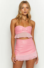 Pink strapless crop top with a sweetheart neckline, small bow detail, and sheer ruffled peplum hem