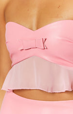 Close-up of the pink faux leather bow detail on the sweetheart neckline of a strapless crop top with a sheer peplum
