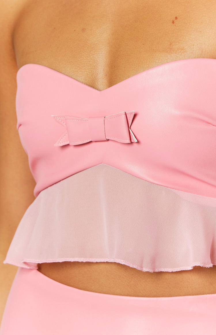 Close-up of the pink faux leather bow detail on the sweetheart neckline of a strapless crop top with a sheer peplum