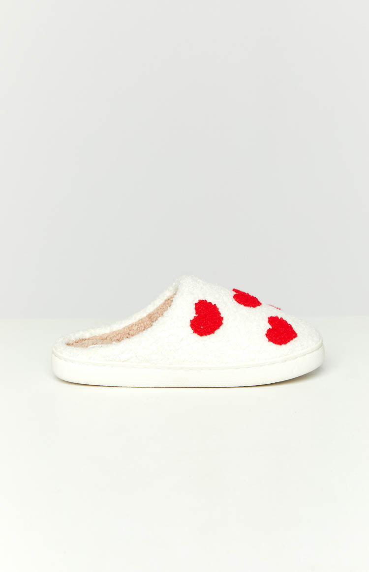 Side view of a white fluffy slipper with red heart patterns and a beige fleece interior