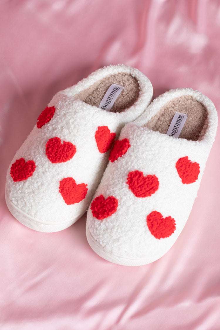 White textured slippers with red heart appliques, showing the beige plush lining and brand tag