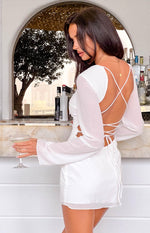 Rear view of a white mini dress with sheer long sleeves, an open back with criss-cross straps and tie detail
