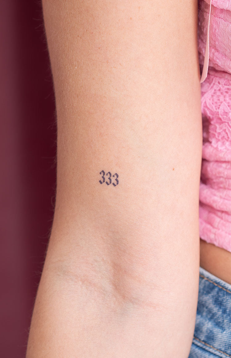 Close-up of a small black '333' number semi-permanent tattoo on the inner arm