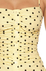 Close-up of the vertical ruching and clear button-front placket on the yellow polka dot mini dress