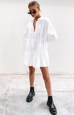 Relaxed fit white mini dress with a collared V-neck, long cuffed sleeves, and gathered tiers