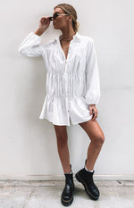 White crinkle fabric long sleeve shirt dress with a collared V-neck, button-front, and three gathered tiers