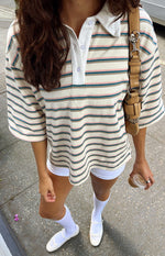 High angle view of the relaxed fit cream polo shirt with green, pink, and brown stripes and elbow-length sleeves