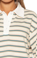 Close-up of the cream polo shirt's white collar, three-button placket, and horizontal teal and pink stripes
