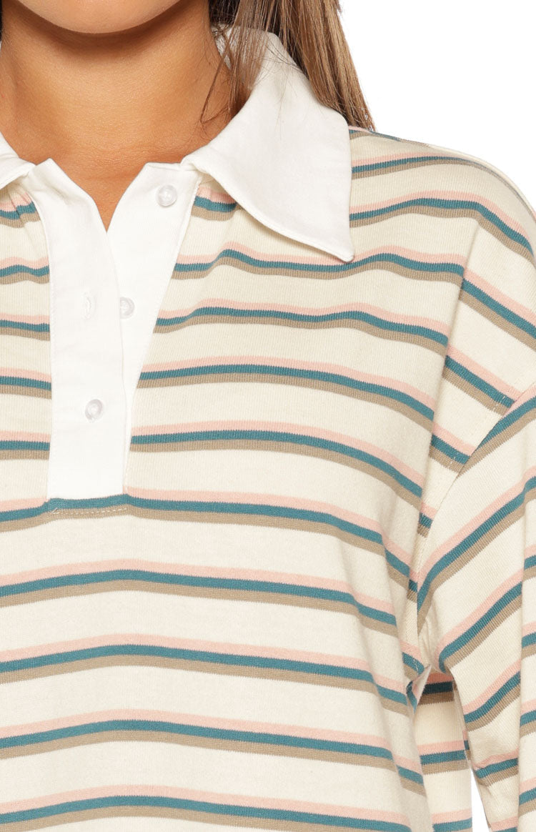 Close-up of the cream polo shirt's white collar, three-button placket, and horizontal teal and pink stripes