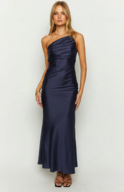 Front view of a navy one-shoulder maxi dress with a draped and ruched bodice and a smooth flowing maxi skirt