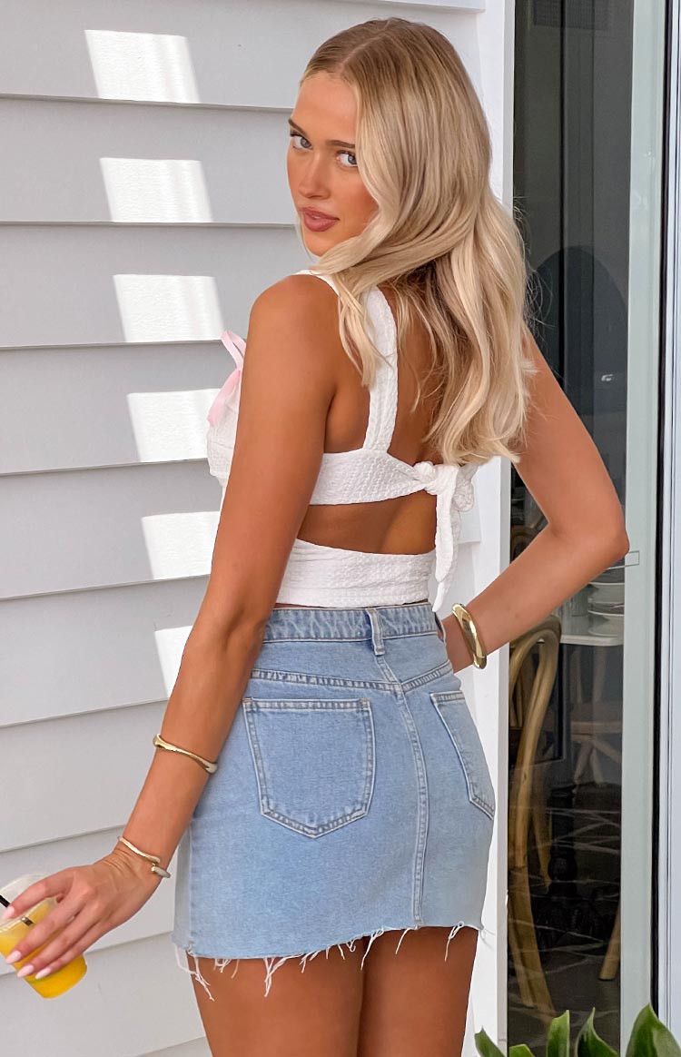 Rear view of a white textured crop top with a back tie closure, cutout detail, and pink bow on the shoulder