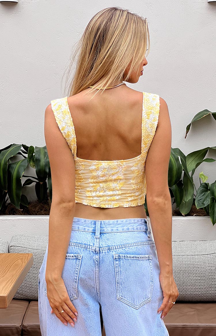 Front view of a yellow lace crop top with a square neckline, wide straps, and small white bows