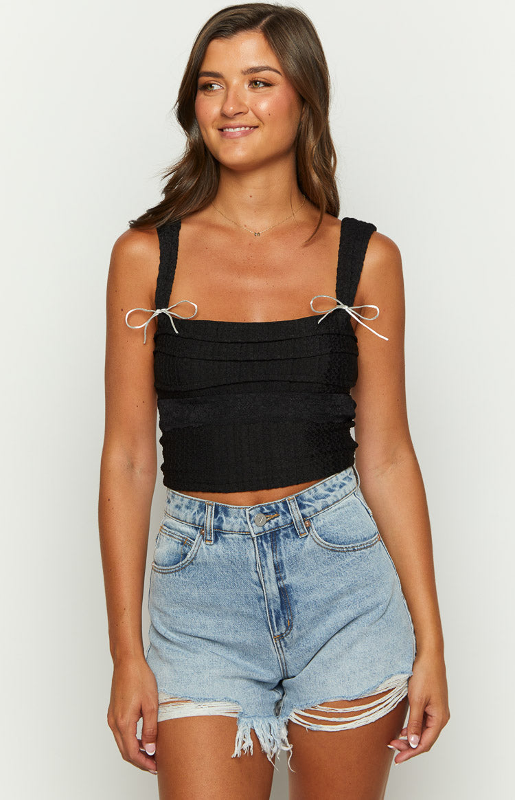 Front view of a black textured crop top with a square neckline and pink bow details on the shoulder straps