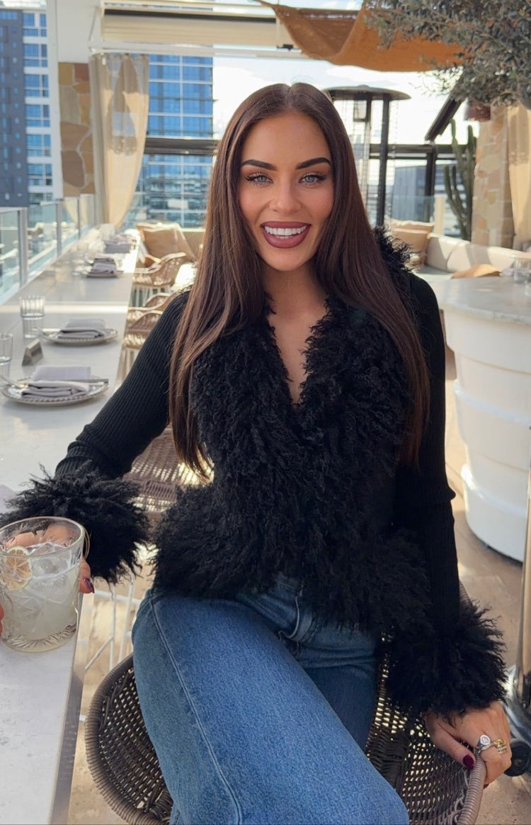 Front view of a black knit cardigan with shaggy fur trim on the V-neck and cuffs, ribbed sleeves
