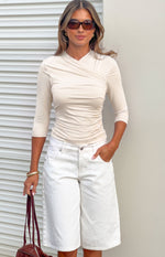 Front view of a cream jersey wrap top with a V-neck, 3/4 sleeves, and gathered ruching on the torso