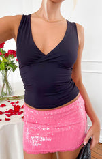 Close-up front view of a pink sequin mini skirt with a visible waistband and lace trim at the hem