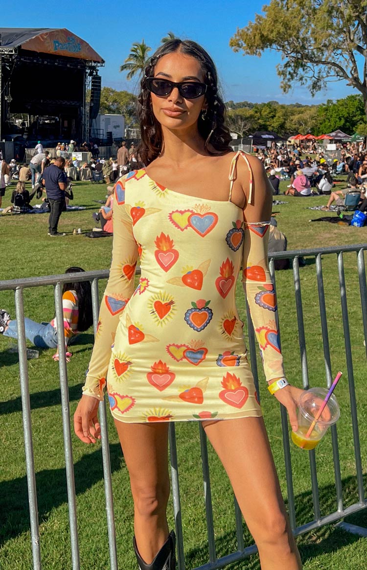 Beginning Boutique Wild At Heart Yellow Printed Mesh Long Sleeve Mini Dress yellow mesh mini dress with sacred heart print, one long sleeve and one tie strap