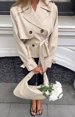 Cream cropped trench coat with double-breasted front, notched lapels, storm flap, shoulder epaulettes, and tied waist belt