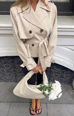 Cream cropped trench coat with double-breasted front, notched lapels, storm flap, shoulder epaulettes, and tied waist belt