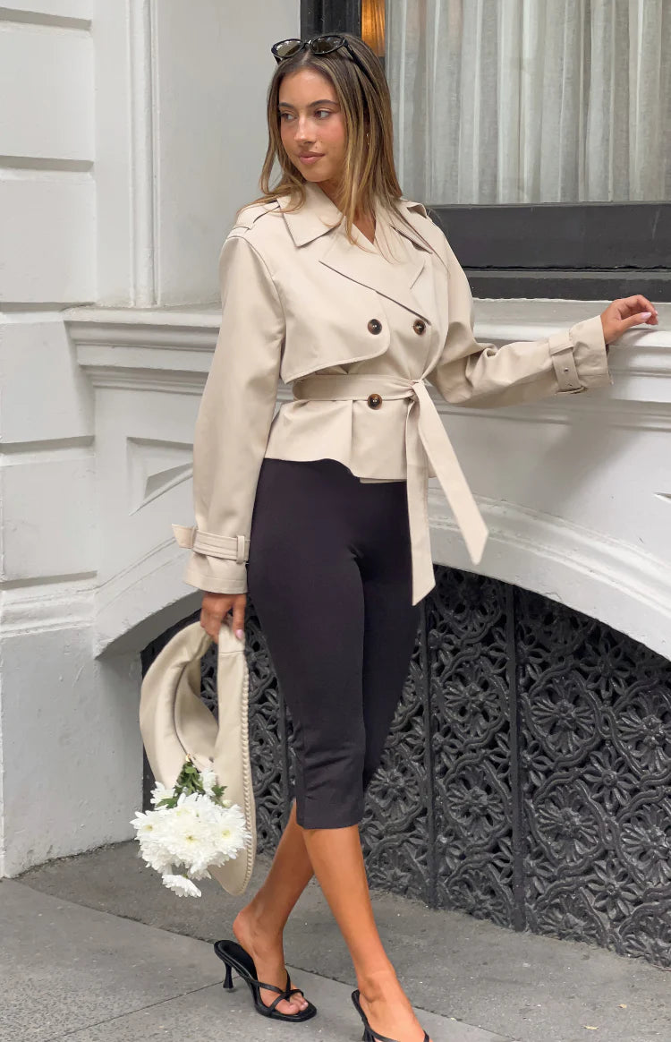 Side view of a cream cropped trench coat with a tied waist belt and adjustable cuff straps