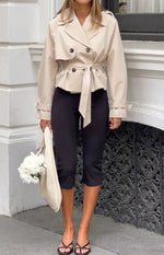 Front view of a cream cropped trench coat with a double-breasted front and cinched waist tie