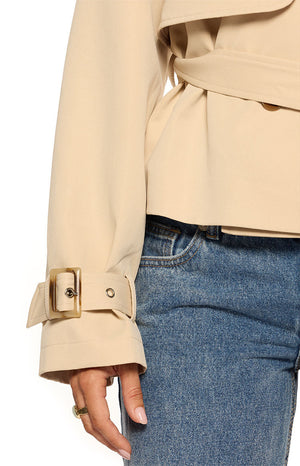 Close-up of the cream cropped trench coat's sleeve with a buckled cuff and tortoise shell buckle
