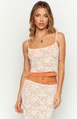 Front view of a white floral lace tank top with orange contrast trim on the neckline and hem