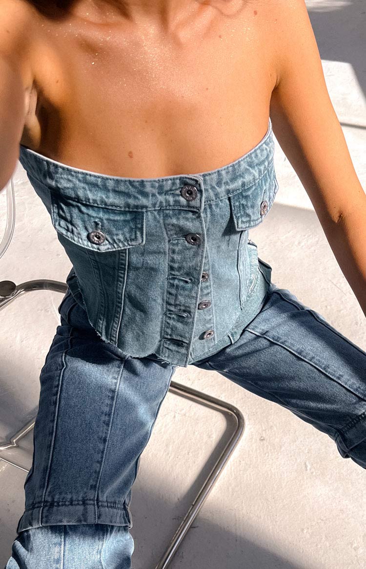 Close-up of the side of a mid-wash denim button top, showing unfastened silver buttons and a raw frayed hem