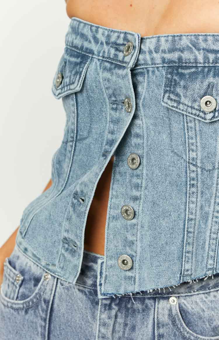 Close-up of the mid wash denim strapless top with button-front closure, chest flap pockets, and raw frayed hem