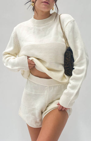 Close-up of the cream knit fabric of a long sleeve top showing the fine texture and crew neckline
