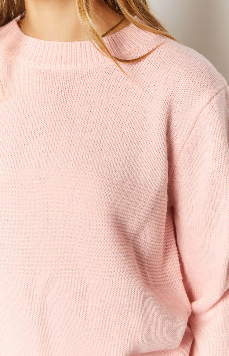 Close-up of the pink long sleeve knit top showing the ribbed crew neck and a textured horizontal knit band
