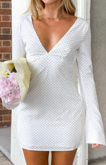 Close-up of the deep V-neckline, fitted bodice, and flared long sleeves of a white polka dot mini dress