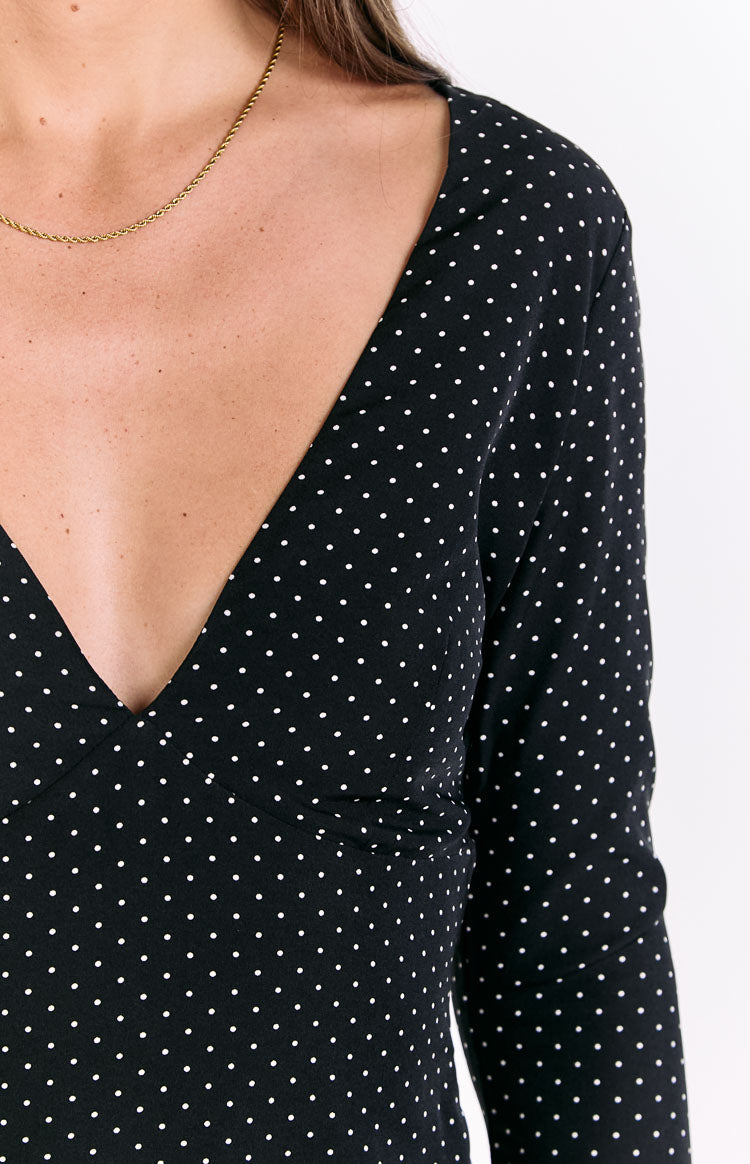 Close-up of the deep V-neckline and shoulder of a black polka dot long sleeve dress
