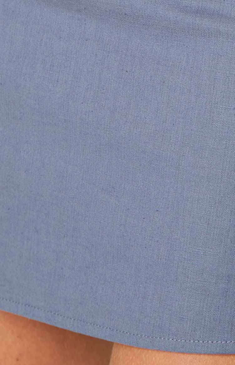 Close-up of the steel blue fabric texture showing the woven material and stitched hem of the mini skirt