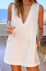 White linen shift mini dress with a deep V-neckline, sleeveless cut, and visible side pocket detail