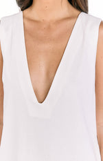 Close-up of the deep V-neckline and sleeveless shoulder of a white linen shift dress