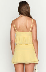 Rear view of a yellow crop top with adjustable spaghetti straps and a ruffled peplum hem