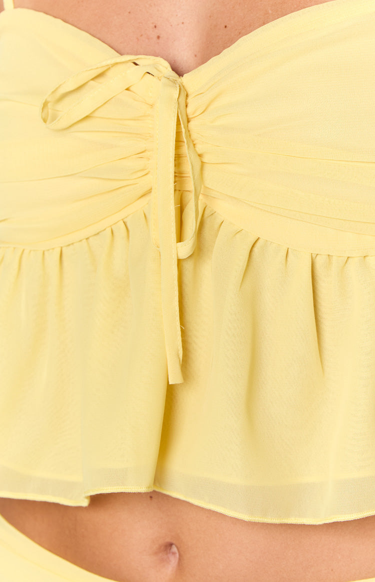 Close-up of the yellow crop top showing the ruched bust with a tie-front detail and flowy hem