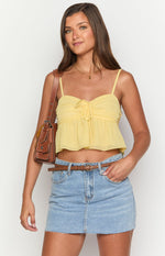 Front view of a sheer yellow crop top with spaghetti straps, a ruched bust, and a tie-front detail