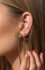 Close-up of the gold bow earring, showing the intricate snake chain texture of the ribbon and long dangling strands