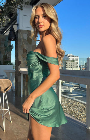 Side view of a green satin off-shoulder mini dress with a ruched bust and flowy skirt