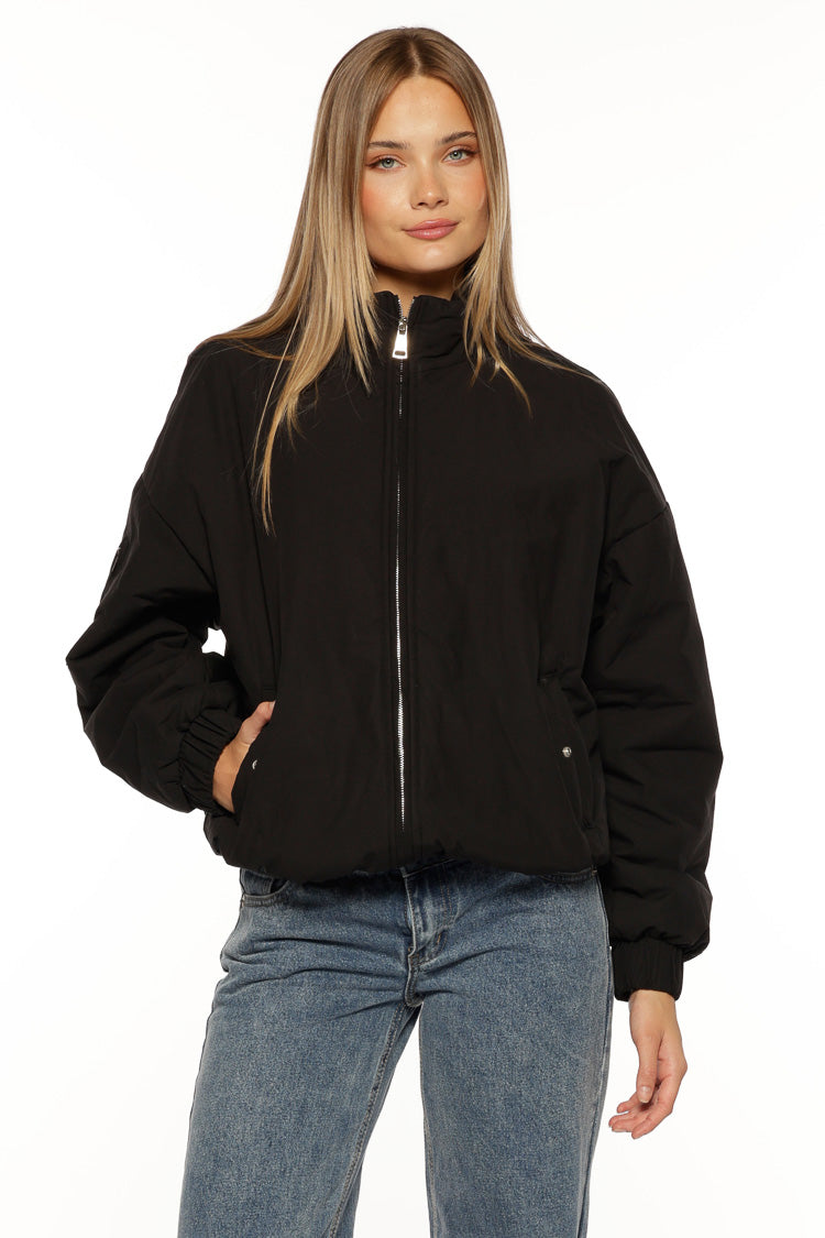 Black oversized puffer jacket showing elasticated cuffs and side pockets with silver snap buttons