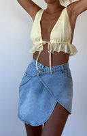 Light wash denim asymmetrical wrap mini skirt with a visible button closure and side pocket